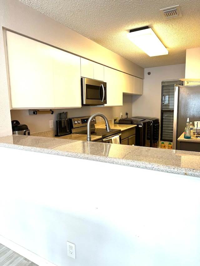 kitchen with light hardwood / wood-style flooring, a textured ceiling, light stone countertops, white cabinetry, and appliances with stainless steel finishes