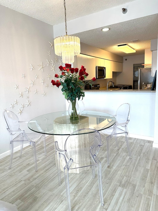 unfurnished dining area featuring an inviting chandelier, sink, a textured ceiling, and light hardwood / wood-style flooring