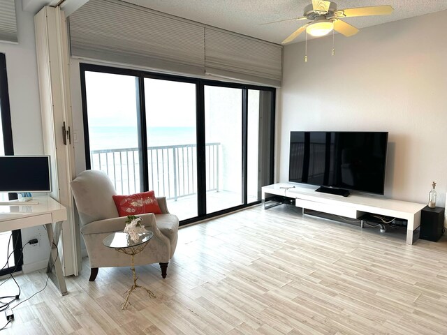 living room with ceiling fan, a textured ceiling, and light wood-type flooring