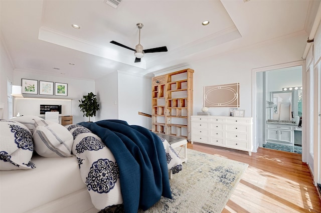 bedroom featuring connected bathroom, light hardwood / wood-style floors, crown molding, and a tray ceiling