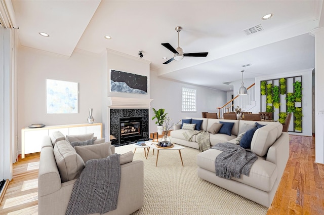 living room with ceiling fan, light hardwood / wood-style floors, crown molding, and a tiled fireplace