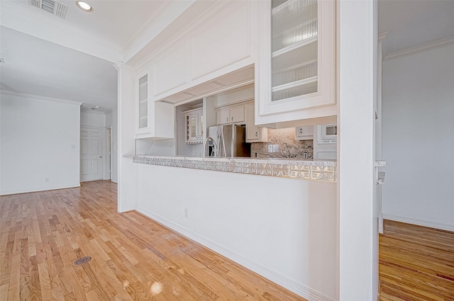 kitchen featuring white cabinets, decorative backsplash, stainless steel fridge, light wood-type flooring, and ornamental molding