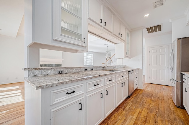 kitchen featuring light stone countertops, light wood-type flooring, stainless steel appliances, sink, and white cabinets