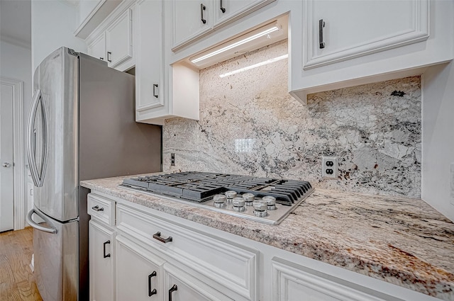 kitchen featuring stainless steel gas stovetop, white cabinets, light stone countertops, tasteful backsplash, and light hardwood / wood-style floors