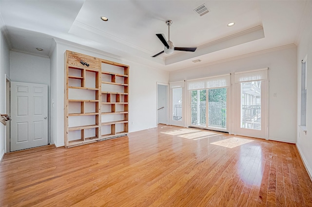 unfurnished living room featuring ceiling fan, light hardwood / wood-style floors, ornamental molding, and a tray ceiling