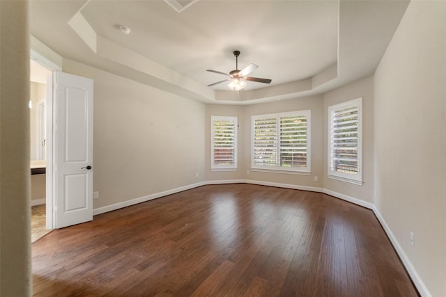 empty room with a tray ceiling, ceiling fan, and dark hardwood / wood-style floors