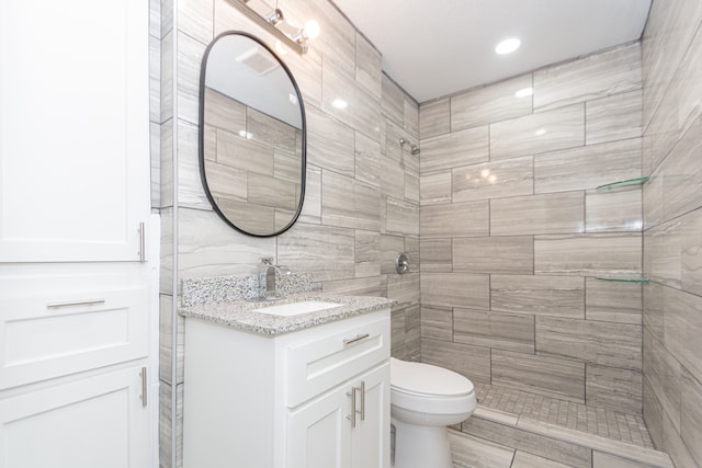 bathroom with tile walls, tiled shower, vanity, and toilet