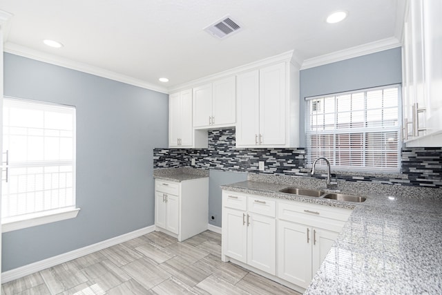 kitchen with white cabinets, a wealth of natural light, sink, and light stone counters