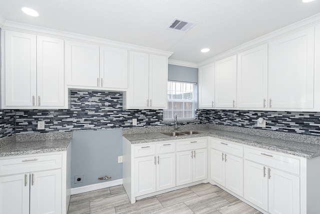 kitchen featuring white cabinets, sink, ornamental molding, backsplash, and light stone countertops