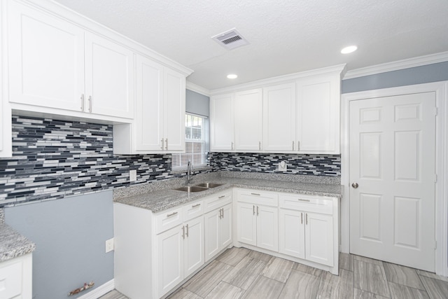 kitchen featuring light stone counters, ornamental molding, backsplash, sink, and white cabinets