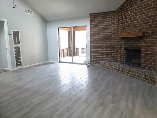 unfurnished living room featuring light wood-type flooring, a brick fireplace, and vaulted ceiling