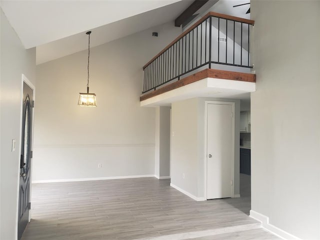 interior space featuring light wood-style floors, baseboards, and high vaulted ceiling