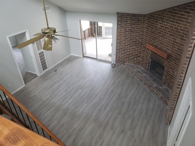 unfurnished living room with a fireplace, hardwood / wood-style flooring, ceiling fan, and brick wall