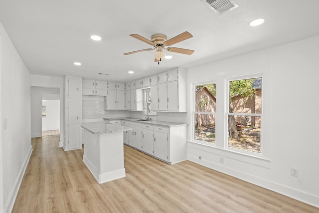 kitchen with sink, light hardwood / wood-style floors, white cabinets, ceiling fan, and a center island