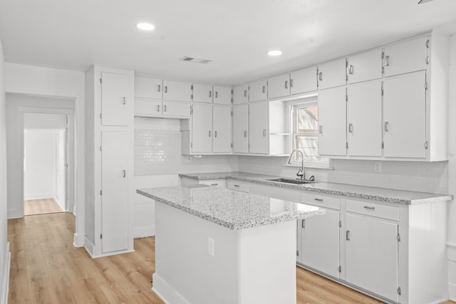 kitchen with a kitchen island, light wood-type flooring, sink, and white cabinets