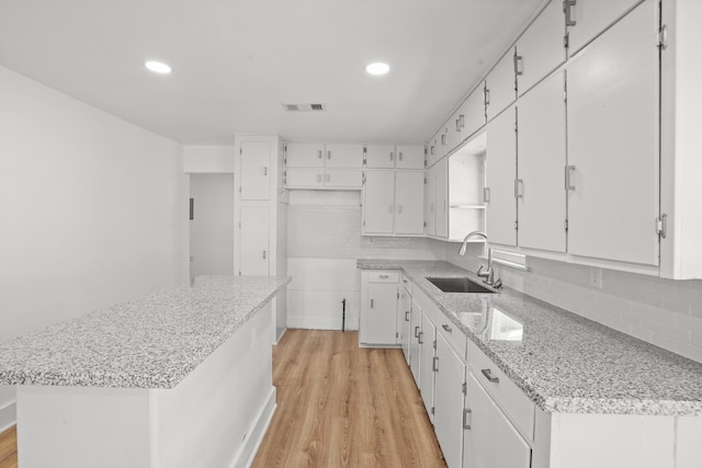 kitchen featuring tasteful backsplash, a center island, sink, white cabinets, and light hardwood / wood-style flooring