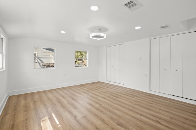 unfurnished bedroom featuring multiple closets, light wood-type flooring, and lofted ceiling