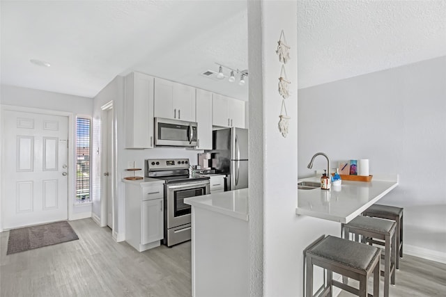 kitchen with white cabinets, stainless steel appliances, a textured ceiling, and light hardwood / wood-style floors