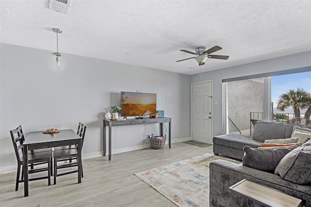 living room with ceiling fan, a textured ceiling, and light wood-type flooring