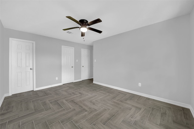 unfurnished bedroom featuring multiple closets, dark parquet flooring, and ceiling fan