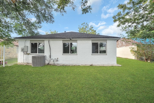 rear view of house featuring central air condition unit and a lawn