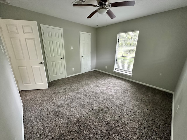 unfurnished bedroom featuring ceiling fan, two closets, and dark carpet