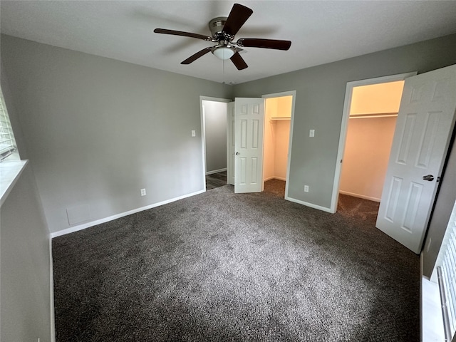 unfurnished bedroom featuring ceiling fan, dark carpet, a walk in closet, and a closet