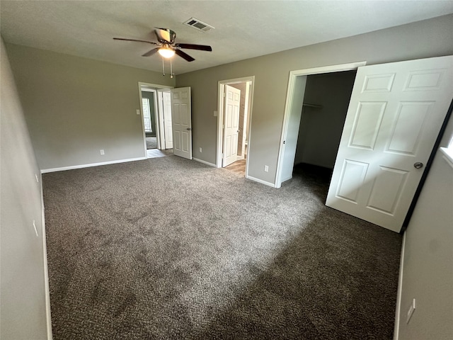 unfurnished bedroom with ceiling fan, dark colored carpet, a closet, and a spacious closet