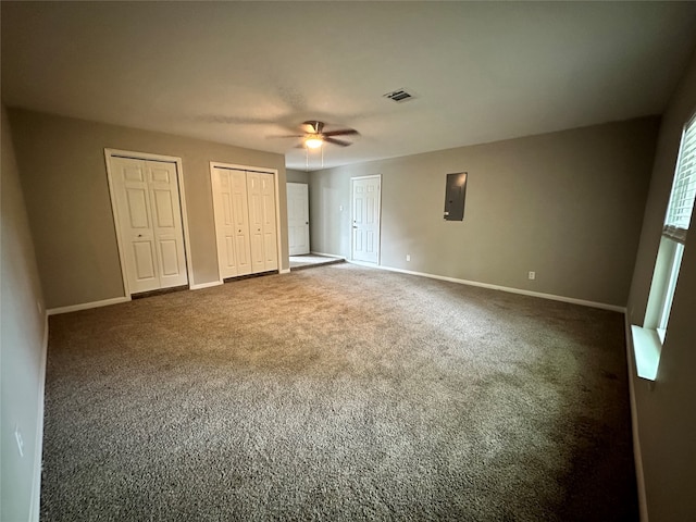 unfurnished bedroom featuring dark colored carpet, electric panel, two closets, and ceiling fan