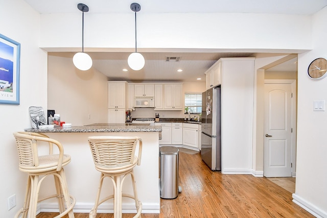 kitchen featuring white cabinets, a kitchen breakfast bar, hanging light fixtures, stainless steel fridge, and kitchen peninsula