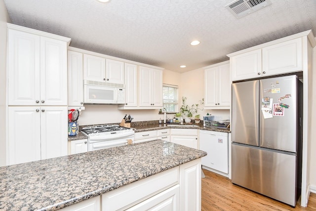 kitchen with white appliances, dark stone counters, white cabinets, light hardwood / wood-style flooring, and a textured ceiling