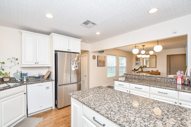 kitchen with dark stone counters, white dishwasher, a textured ceiling, white cabinetry, and stainless steel refrigerator