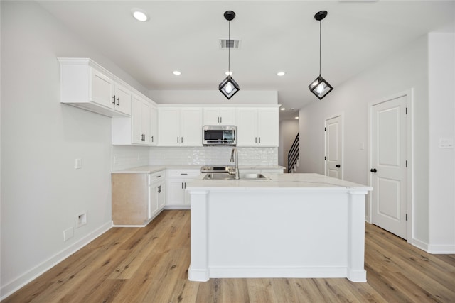 kitchen with sink, an island with sink, light hardwood / wood-style flooring, white cabinets, and pendant lighting