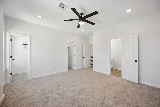 unfurnished bedroom with a spacious closet, light carpet, ceiling fan, and connected bathroom