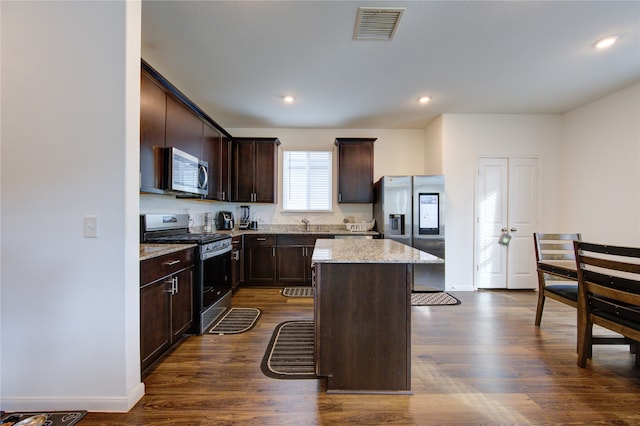 kitchen with dark wood-type flooring, light stone counters, a center island, dark brown cabinets, and appliances with stainless steel finishes