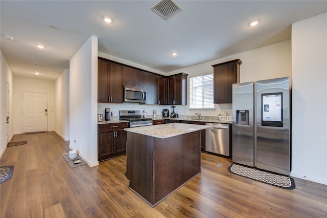 kitchen with stainless steel appliances, dark hardwood / wood-style flooring, light stone counters, a center island, and dark brown cabinetry