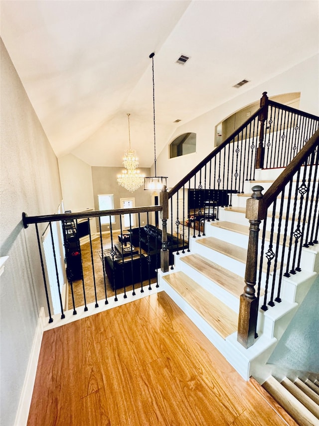 stairs with hardwood / wood-style floors, vaulted ceiling, and a notable chandelier