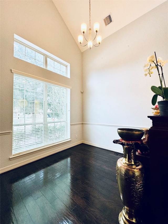 empty room featuring high vaulted ceiling, plenty of natural light, a notable chandelier, and hardwood / wood-style flooring