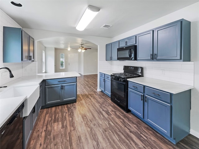 kitchen with black appliances, kitchen peninsula, ceiling fan, blue cabinets, and dark wood-type flooring