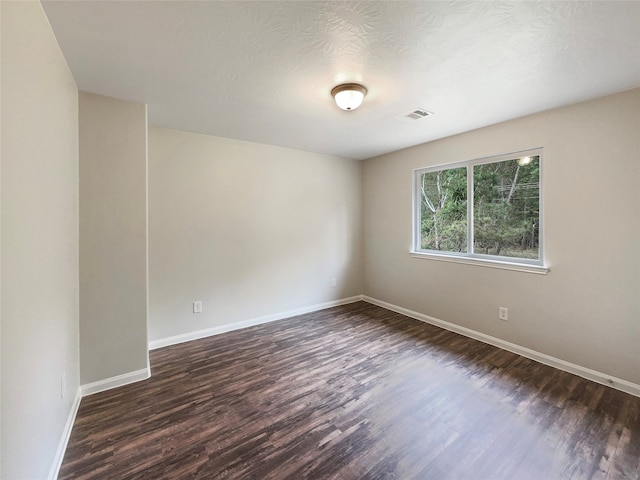 spare room with a textured ceiling and dark hardwood / wood-style flooring