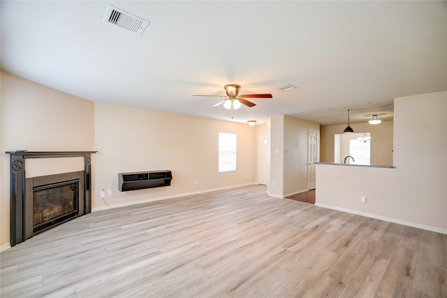 unfurnished living room with ceiling fan, heating unit, sink, and light wood-type flooring