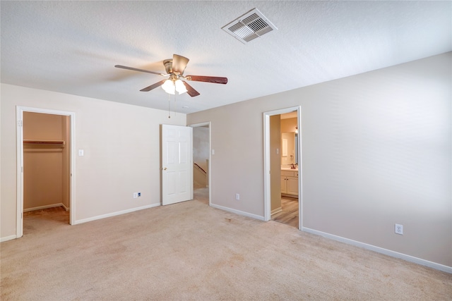 unfurnished bedroom with a closet, a walk in closet, ensuite bath, light carpet, and ceiling fan