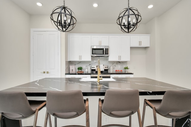 kitchen with white cabinetry, decorative backsplash, an island with sink, and an inviting chandelier