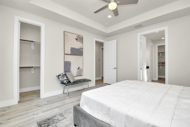 bedroom with a closet, light wood-type flooring, a walk in closet, and ceiling fan