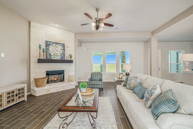 living room with ceiling fan, a stone fireplace, and dark hardwood / wood-style flooring