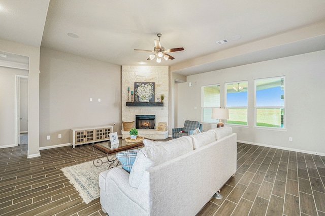 living room featuring a stone fireplace, dark wood-type flooring, and ceiling fan