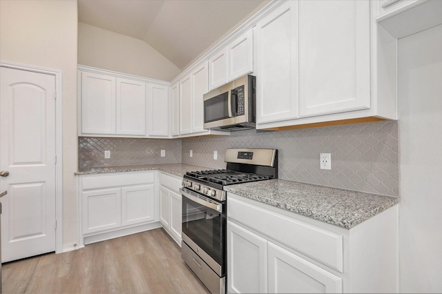 kitchen with appliances with stainless steel finishes, tasteful backsplash, light stone countertops, lofted ceiling, and white cabinets