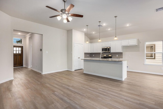 kitchen featuring white cabinetry, appliances with stainless steel finishes, light stone countertops, a kitchen island with sink, and light hardwood / wood-style flooring