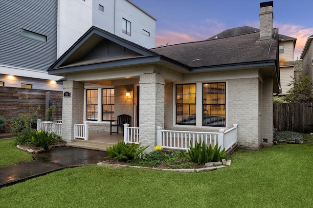 back house at dusk featuring covered porch and a yard