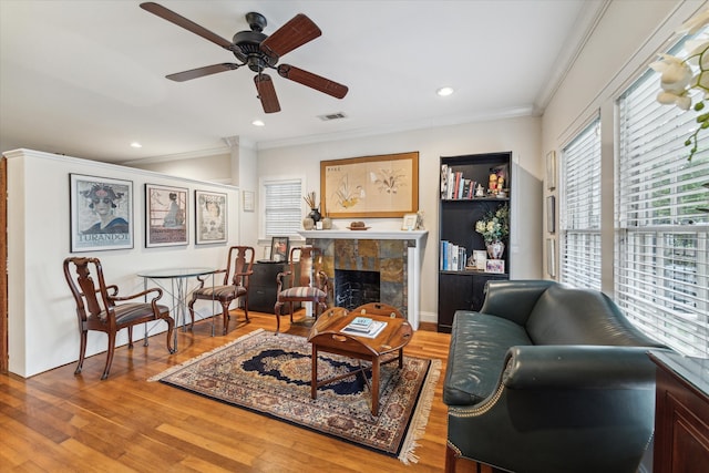 living room featuring ceiling fan, a tile fireplace, hardwood / wood-style flooring, and ornamental molding